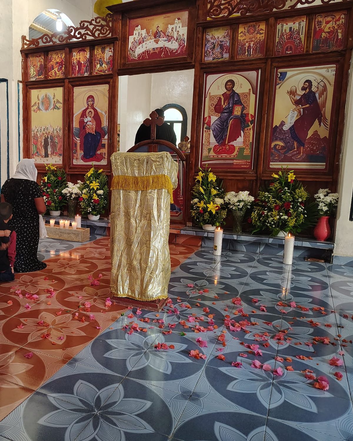 An Orthodox church with an iconostasis of painted icons, a Gospel stand, candles and flowers
